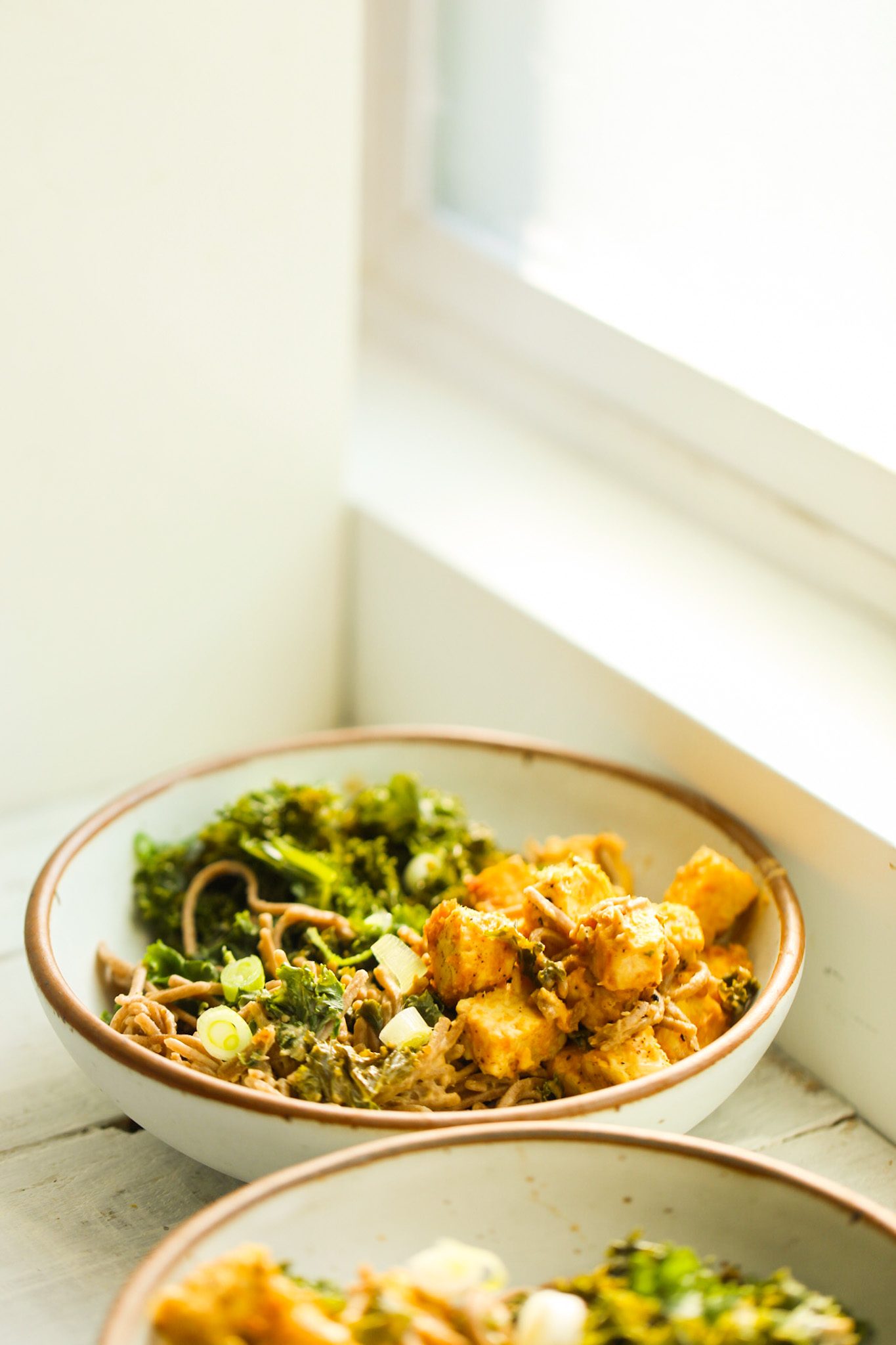 Peanut sauce-coated noodles with tempeh cubes and wilted kale in a bowl.