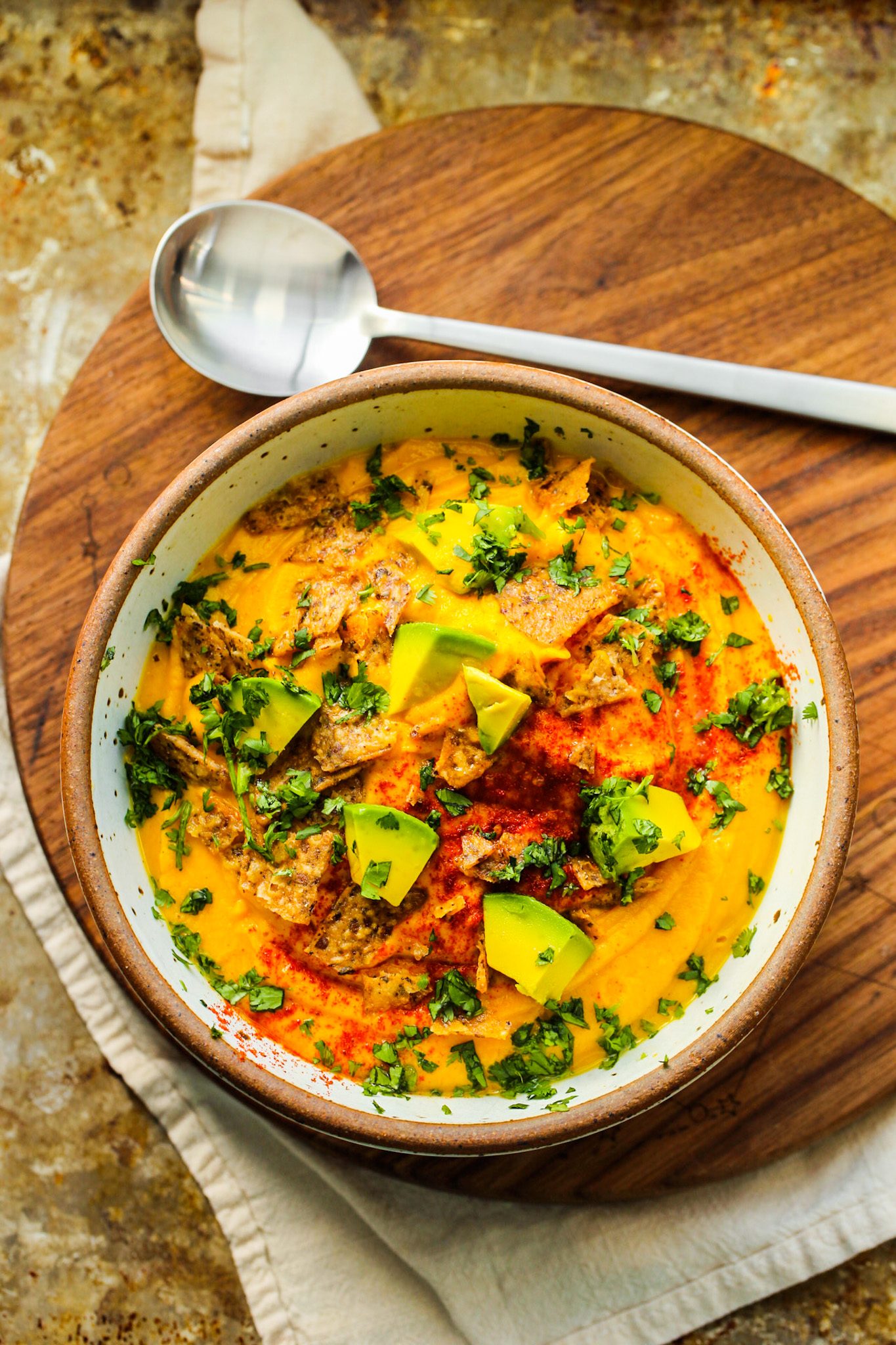 Creamy sweet potato cauliflower soup topped with diced avocado, herbs, smoky paprika and crushed chips.