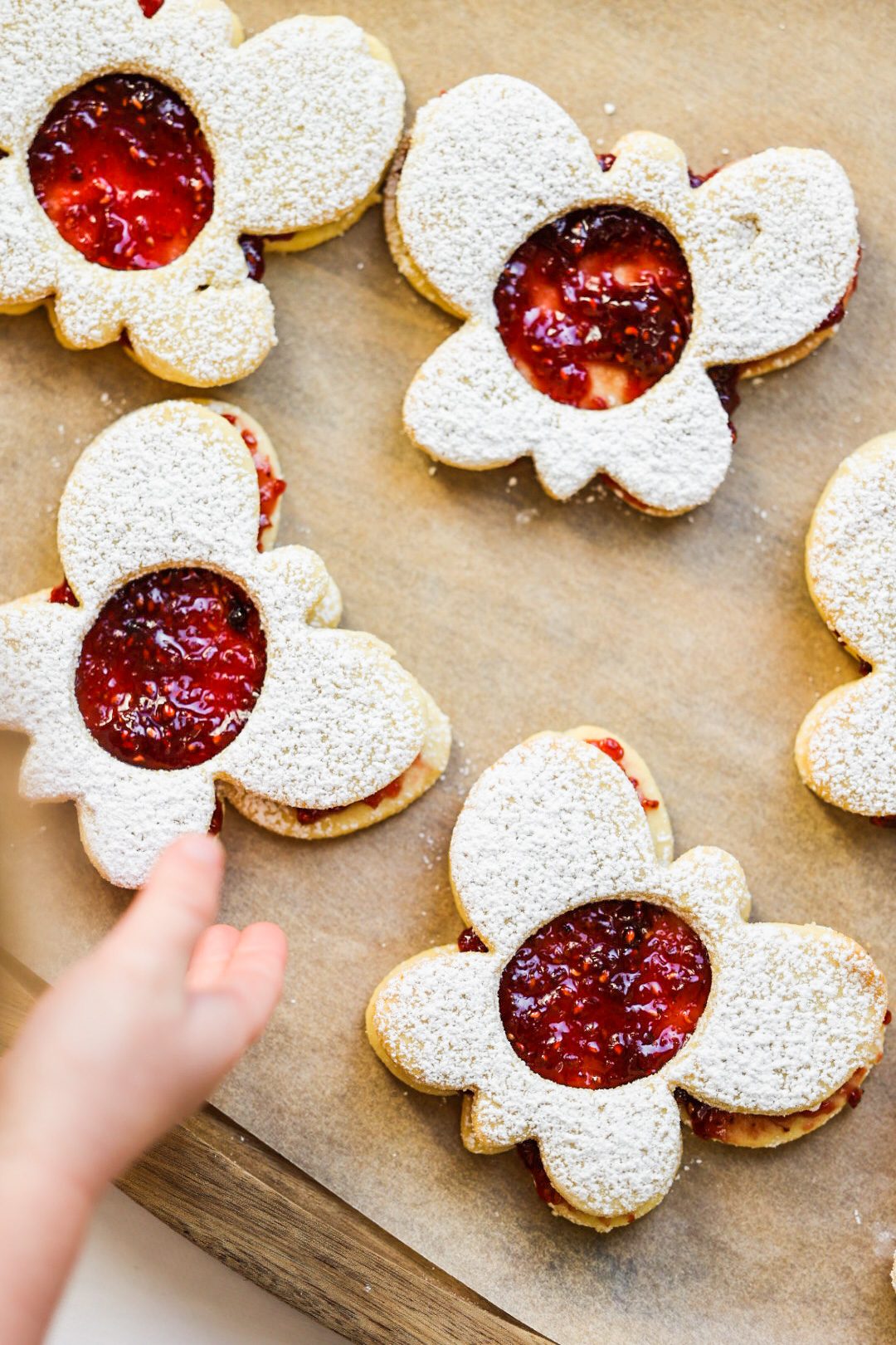Butterfly-shaped vegan Linzer cookies dusted with powdered sugar, with raspberry jam peeking through their centers.