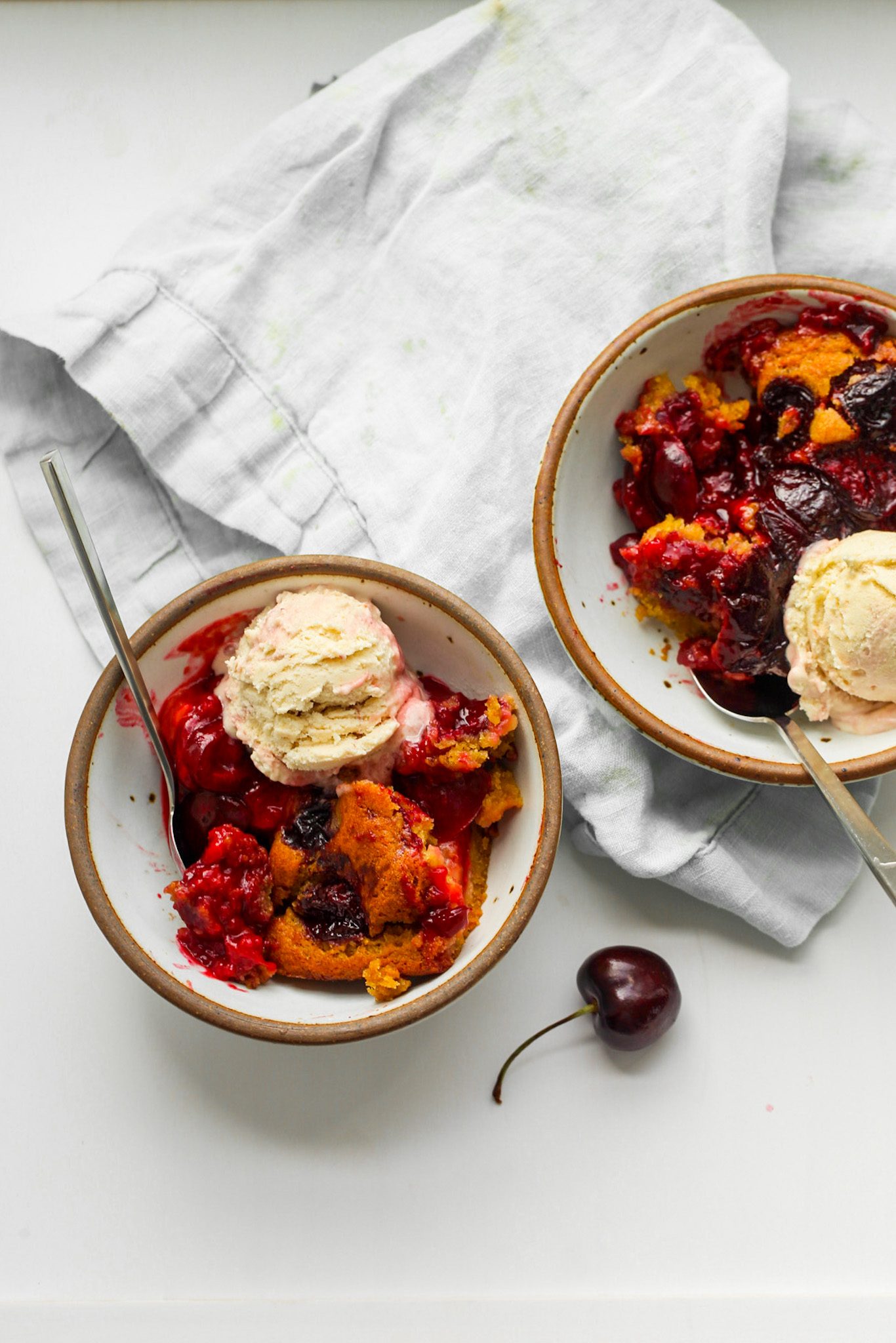 Fresh cherry cobbler with deep red cherry filling and fluffy cake, served with a scoop of vegan ice cream.