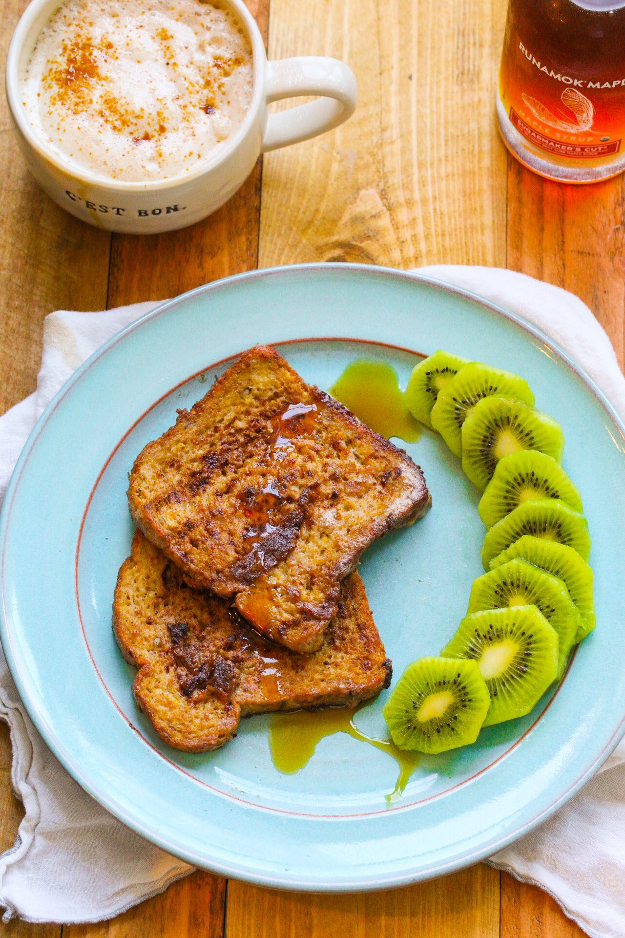 Vegan banana French toast with lightly browned edges, maple syrup and sliced kiwi on a turquoise plate.