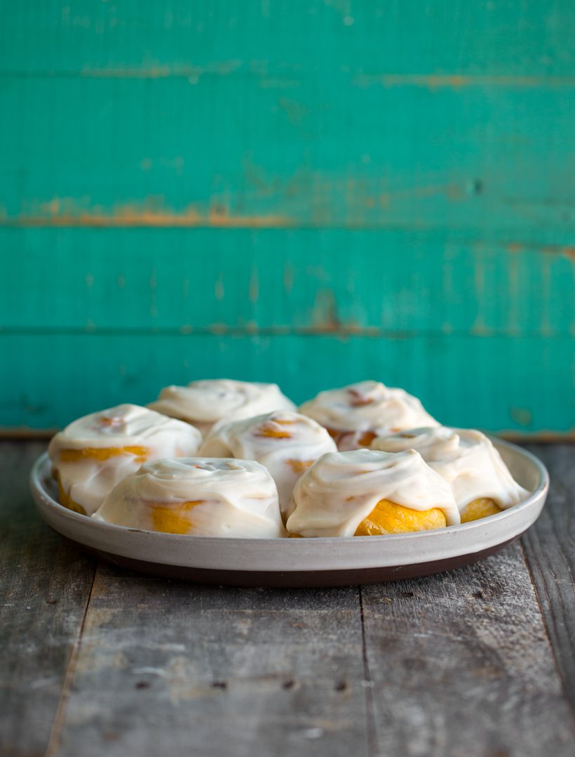 Fluffy pumpkin cinnamon rolls with cinnamon-sugar swirls and white vegan cream cheese frosting.