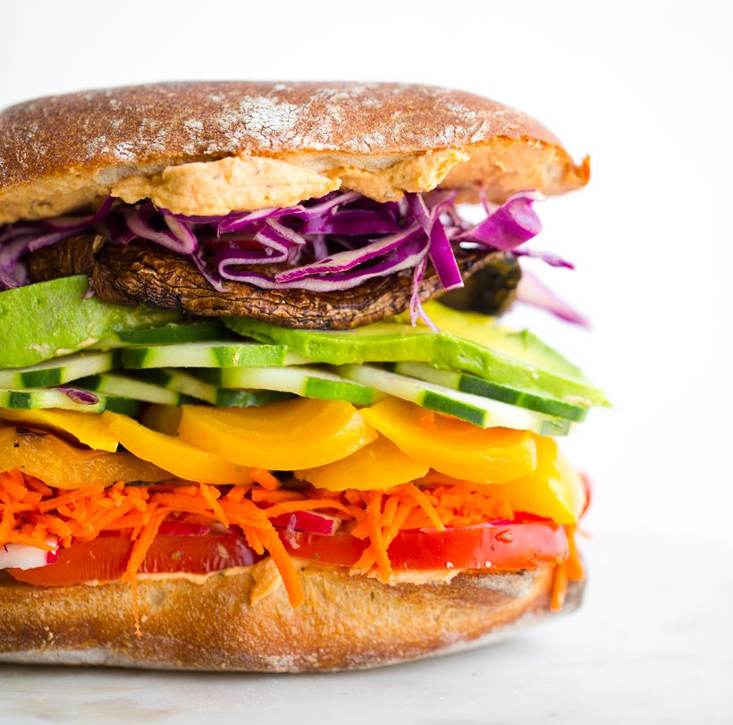 A rainbow veggie sandwich layered with colorful vegetables, avocado and hummus on a ciabatta-style roll.