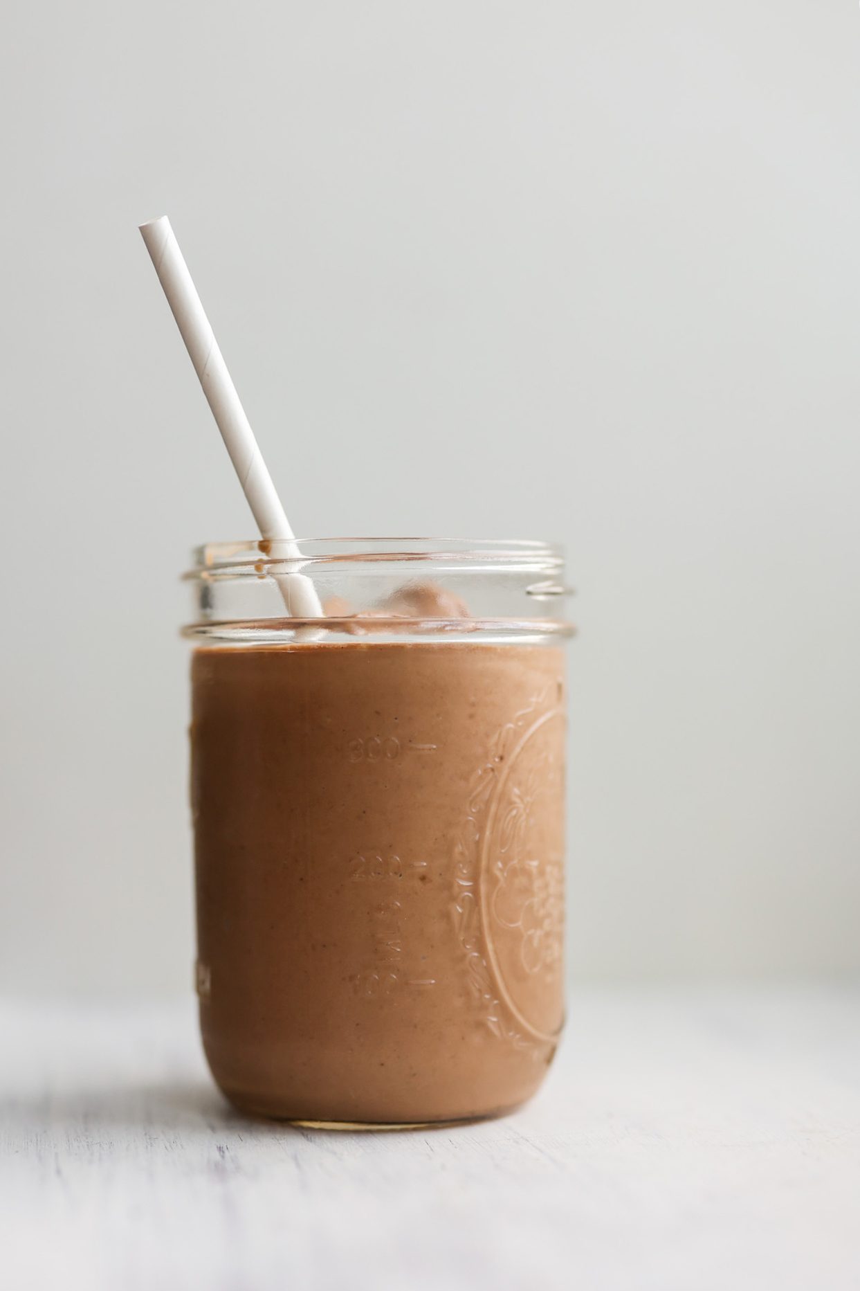 A frosty, creamy chocolate protein shake made with bananas and dairy-free milk, served with a straw.