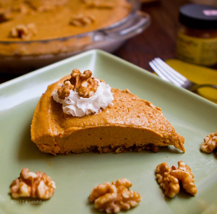 Creamy pumpkin pie with a rustic walnut crust, topped with a swirl of soy whipped cream and walnut accents.