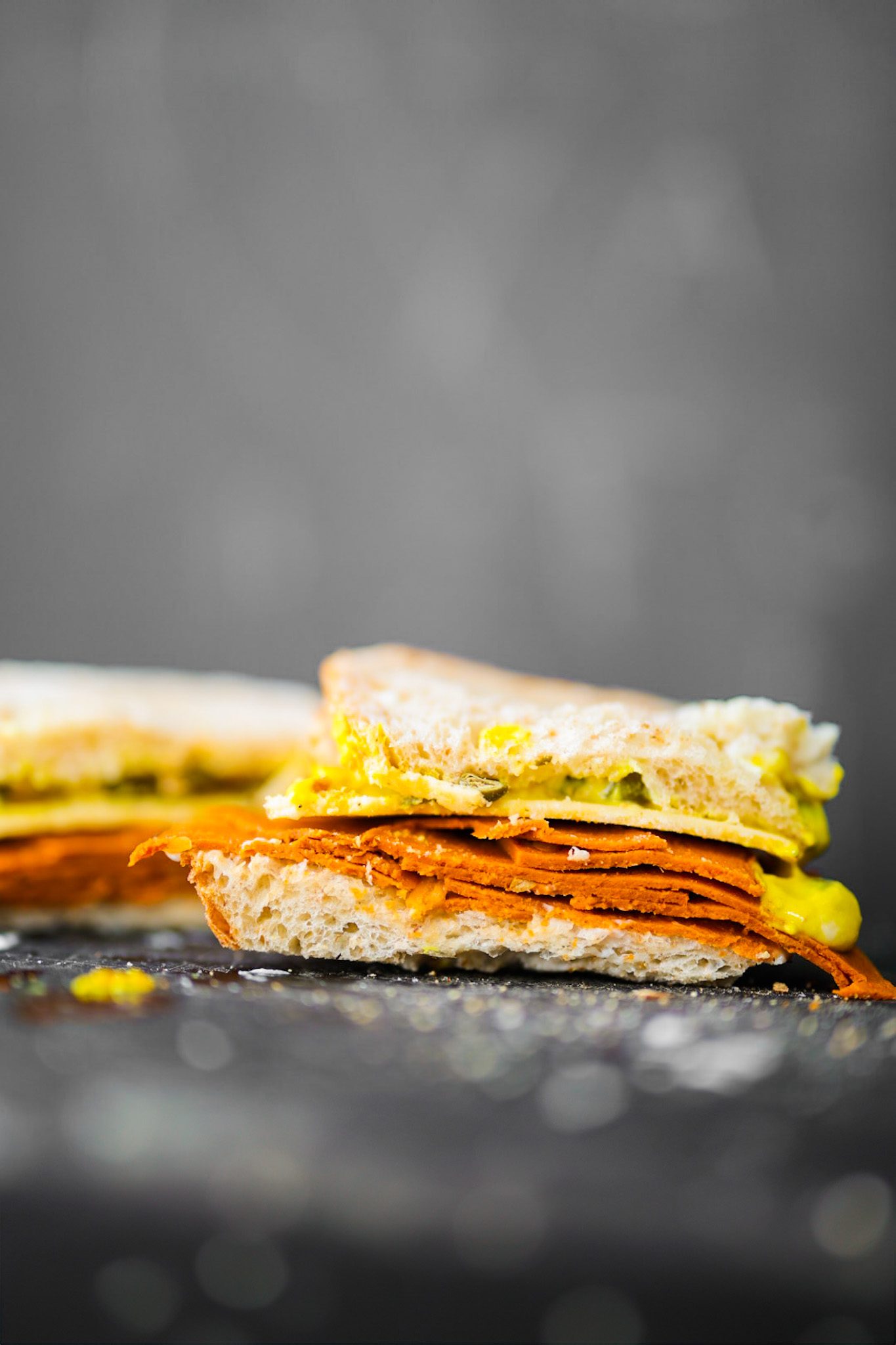 A vegan lunchmeat and cheese sandwich on sourdough bread with plant-based mayo and yellow mustard.