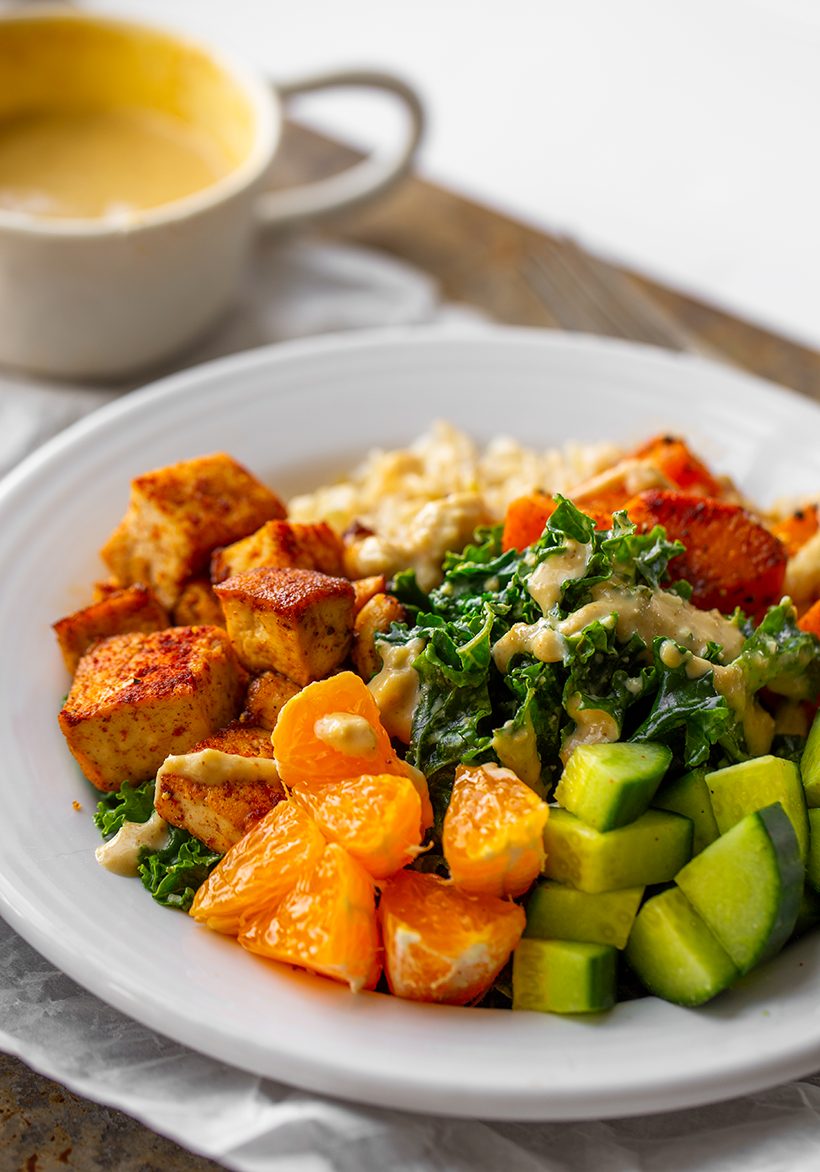 A vegan Buddha bowl with smoky maple tofu, sweet potatoes, brown rice, kale, cucumber, mandarin orange, cashews and creamy cashew dressing.