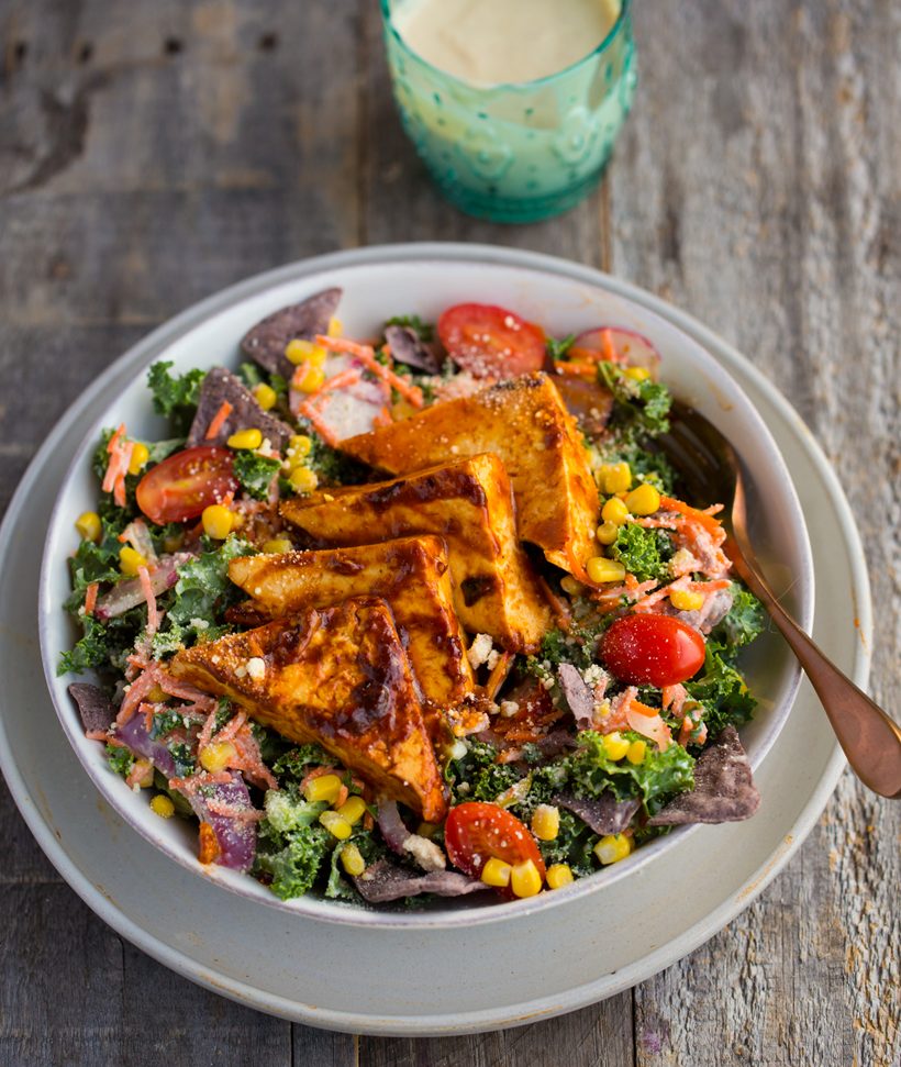 Kale salad with corn, carrots, radishes and tomatoes, topped with sticky BBQ tofu triangles and creamy vegan ranch dressing.