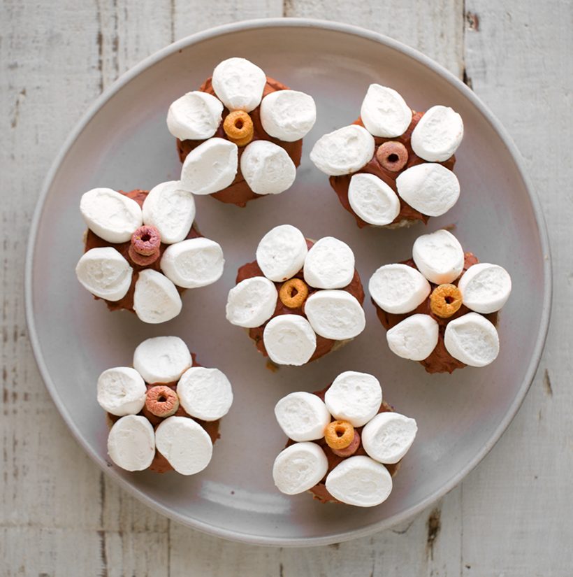 Vegan funfetti cupcakes topped with chocolate frosting and white marshmallow flower petals with colorful cereal centers.
