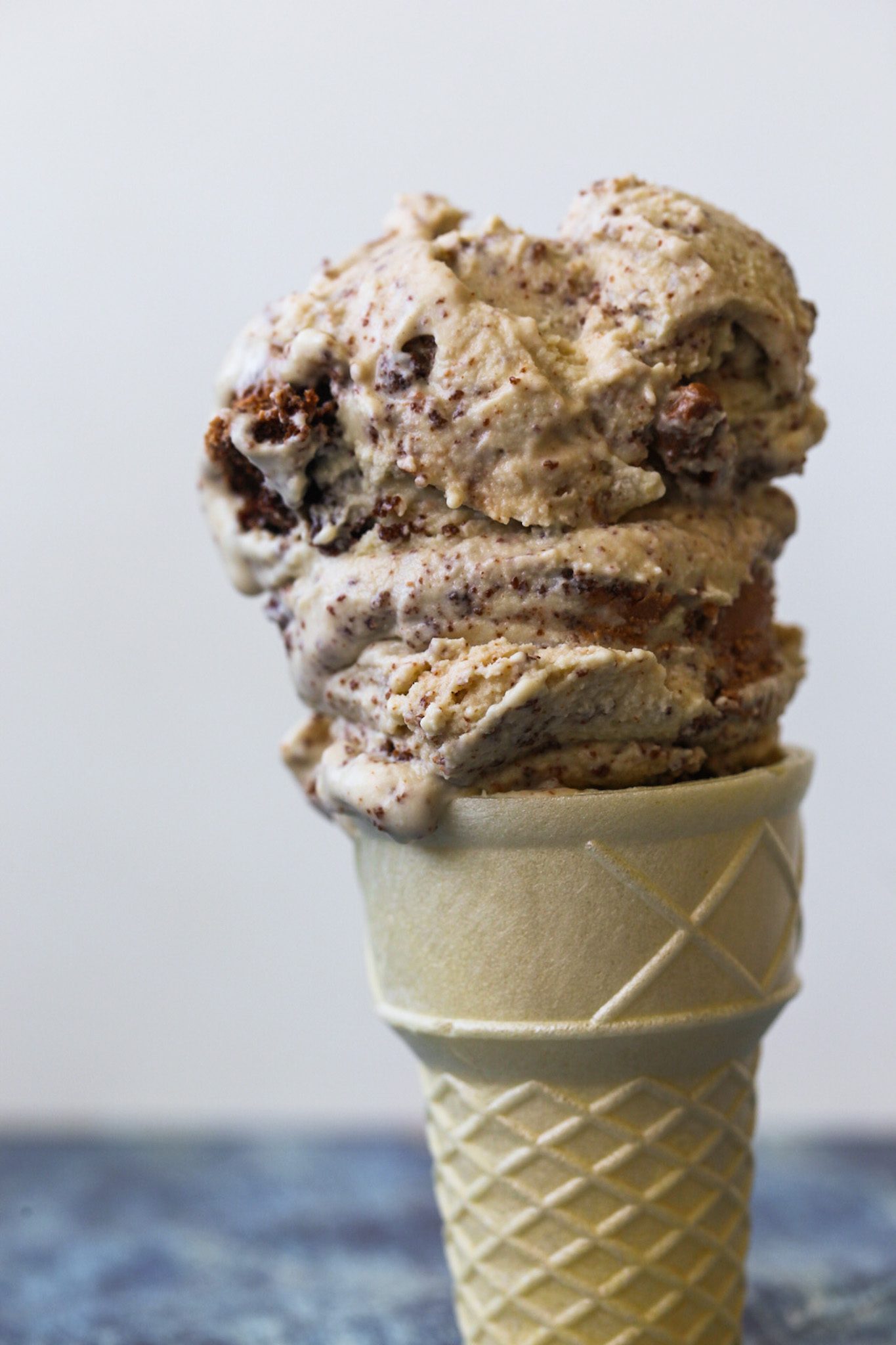 Vanilla cashew ice cream with chunks of vegan chocolate cake, scooped onto a cone.