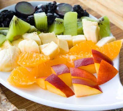 Whole wheat wraps spread with vegan cream cheese and topped with colorful chopped fruit arranged in rainbow rows.