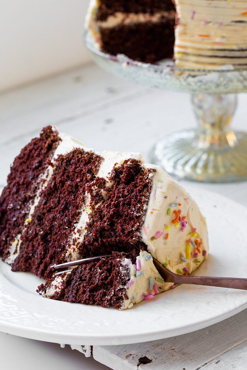 Vegan chocolate layer cake covered in creamy vanilla funfetti frosting and colorful sprinkles.