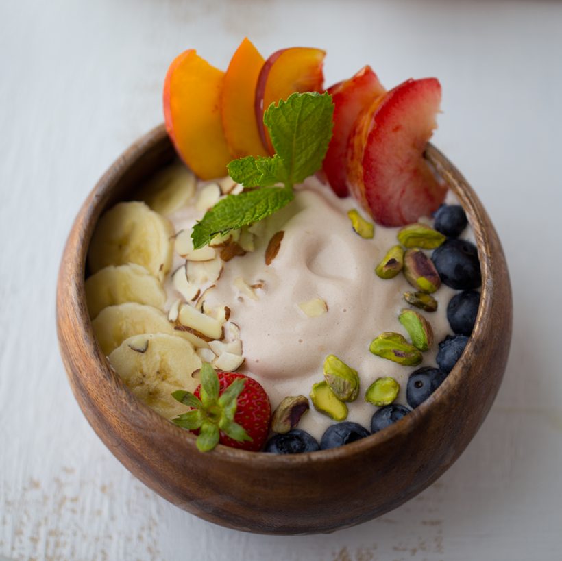 A creamy smoothie bowl topped with fresh fruit, nuts and seeds, alongside tips for making plant-based smoothie bowls.