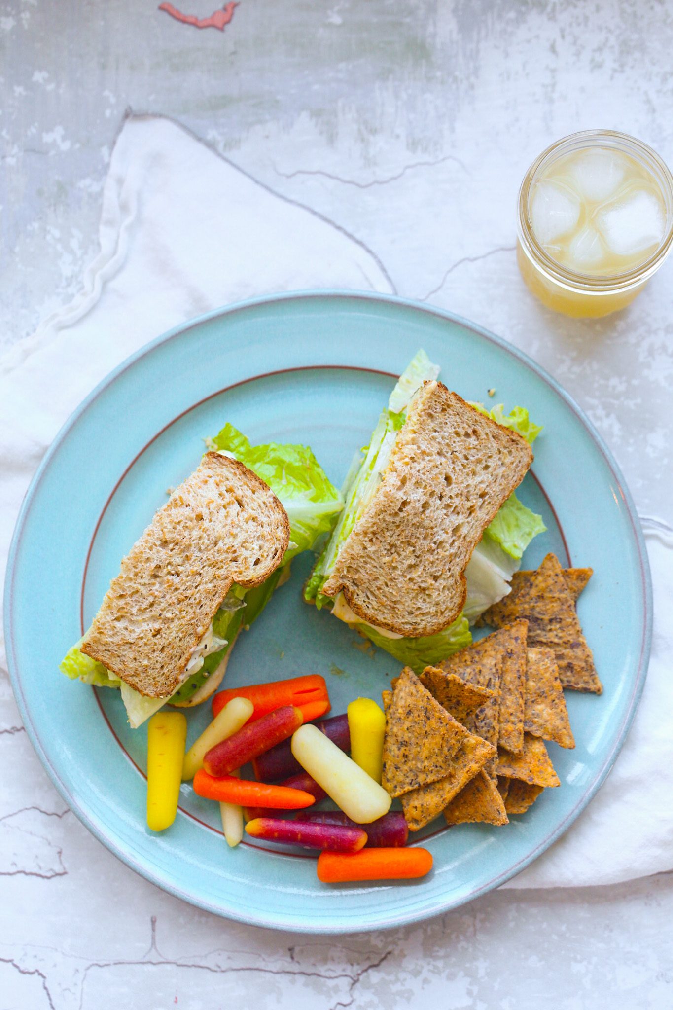 Avocado, hummus, crunchy romaine and pickle sandwich on sprouted grain bread, served with carrots.