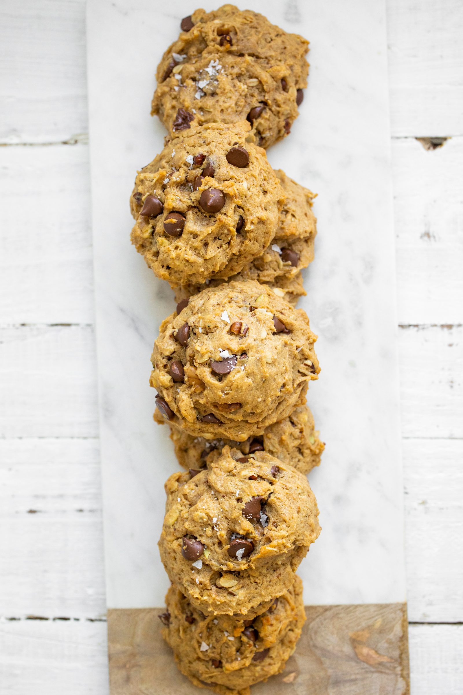 Thick vegan cookies with oats, nuts, pumpkin seeds and melty chocolate chips arranged in a row.