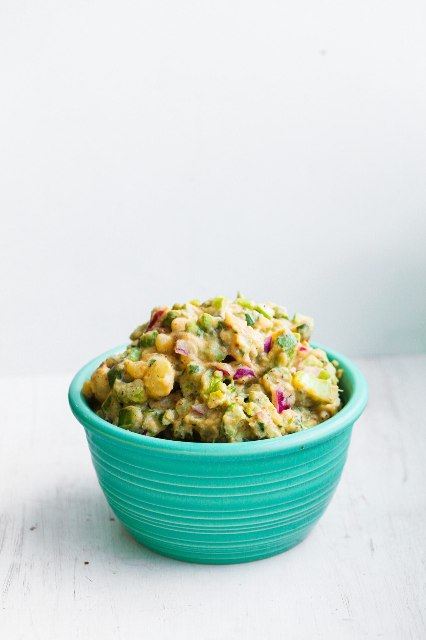 Creamy vegan potato salad with chunky potatoes, celery, red onion, spinach, and pickles in a teal bowl.