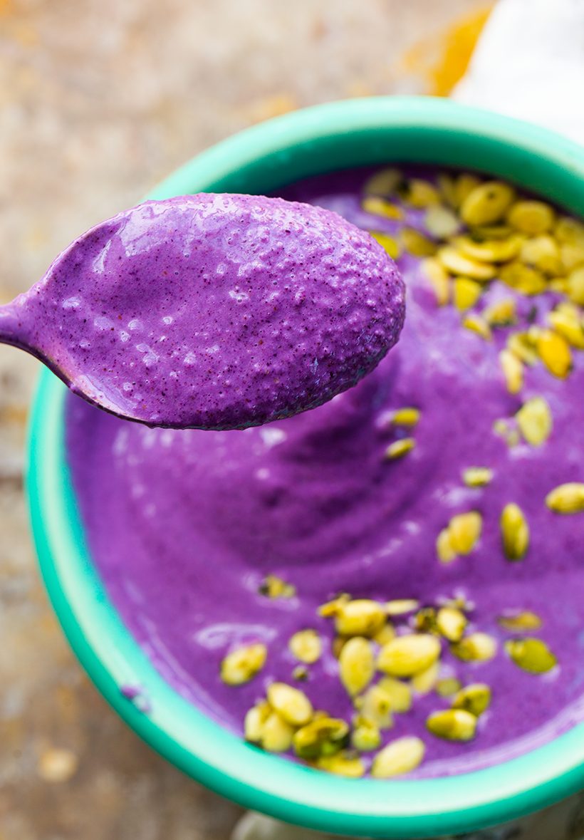 A thick, frosty purple wild blueberry and banana smoothie topped with green pumpkin seeds.