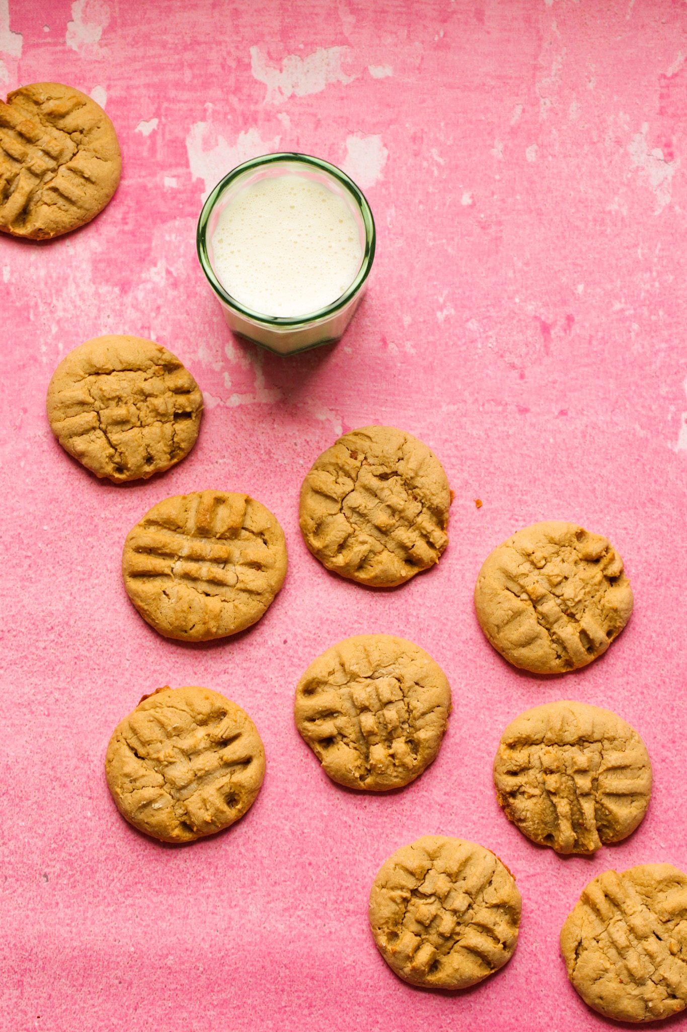 Tender maple peanut butter cookies with fork-pressed crisscross tops, served with a glass of soy milk on a pink surface.