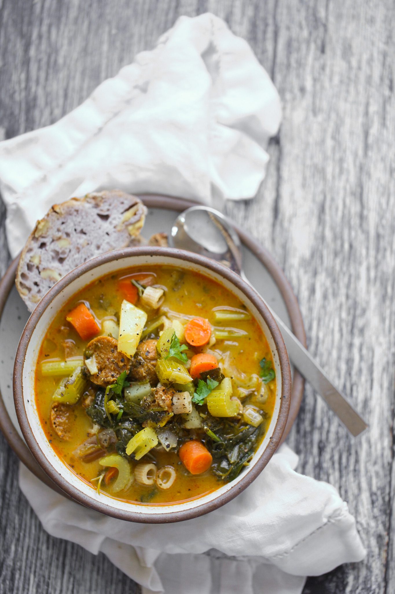 Chunky winter vegetable stew with potatoes, carrots, leafy greens, pasta and vegan sausage, served with crusty bread.