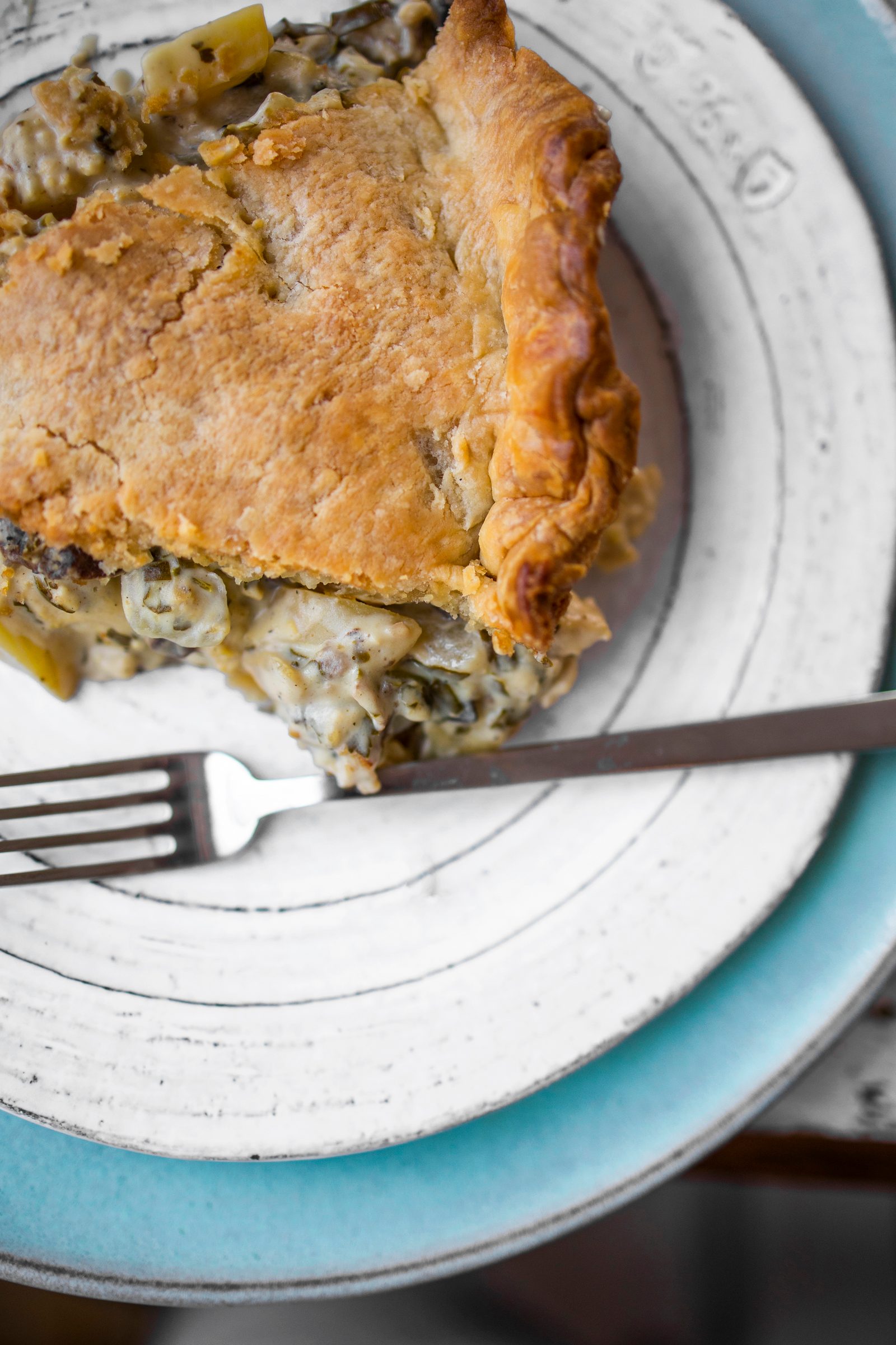 A slice of mushroom potato pot pie with a creamy cashew filling, chunks of tofu, and a golden pastry crust.